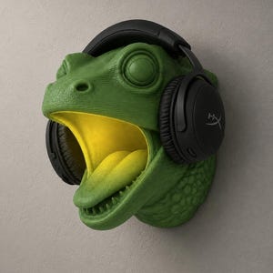 Op de afbeelding: Een groene, getextureerde wandsculptuur van een reptielenkop met een open mond en gele binnenkant. Zwarte koptelefoon met het HyperX-logo is over het hoofd geplaatst. De sculptuur is op een grijze muur gemonteerd.
