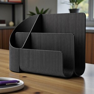 May include: Black desk organizer with a ribbed texture. The organizer has multiple compartments for storing office supplies. It is made of a solid, matte black material and sits on a wooden desk.