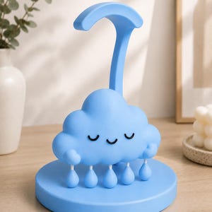May include: A light blue cloud-shaped night light with a curved handle. The cloud has a smiling face with closed eyes and teardrop-shaped rain drops hanging below. The night light sits on a round base.