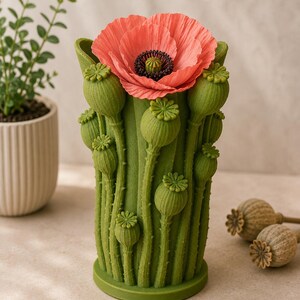 K&ouml;nnte beinhalten: Eine gr&uuml;ne Vase in Form von Mohnst&auml;ngeln mit einer gro&szlig;en korallenfarbenen Mohnblume an der Spitze. Die Vase hat detaillierte Samenkapseln und Stiele. Zwei getrocknete Mohnsamenk&ouml;pfe befinden sich im Hintergrund. Eine dekorative Blumenvase.