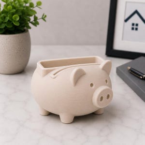 May include: A light beige piggy bank with a slot on top for inserting money. The bank has a rounded body, four small legs, and features like ears, eyes, and a snout. The bank is made of a textured material and is designed to look like a pig.