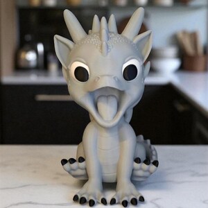 May include: A light gray dragon figurine with large black eyes and an open mouth, revealing a pink tongue. The dragon has spiky features on its head and black claws. It is sitting on a white marble surface.