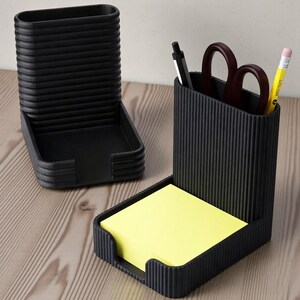 Pu&ograve; includere: Set di organizer da scrivania neri in due pezzi. Una sezione contiene una pila di post-it gialli. L'altra sezione ha una penna, forbici e una matita. Entrambe le sezioni hanno un design a coste.