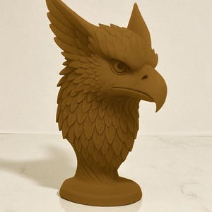 May include: A brown griffin head sculpture. The sculpture features detailed feather and scale textures, with a prominent beak and piercing eye. The griffin has large, upright ears and a detailed mane. The sculpture is mounted on a round base.