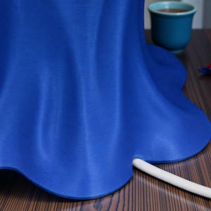 May include: A vibrant blue, petal-shaped object with a white, cylindrical element extending from its base. The object sits on a wooden surface, with a teal cup visible in the background. The object's form suggests a decorative or functional item.