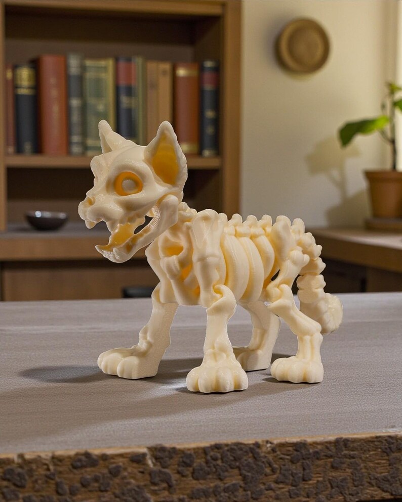 Puede incluir: Figura de esqueleto de gato impresa en 3D, de color crema. La figura tiene una estructura esquel&eacute;tica detallada con costillas, columna vertebral y cr&aacute;neo visibles. Los ojos y las orejas tienen un tono amarillo-anaranjado. El gato est&aacute; en posici&oacute;n de caminar.