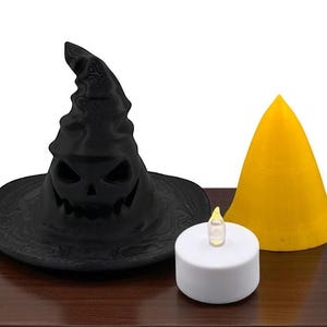 May include: A black Halloween witch hat with a carved jack-o'-lantern face, a yellow cone, and a white battery-operated candle with a flickering yellow flame. The items are arranged on a dark brown surface.
