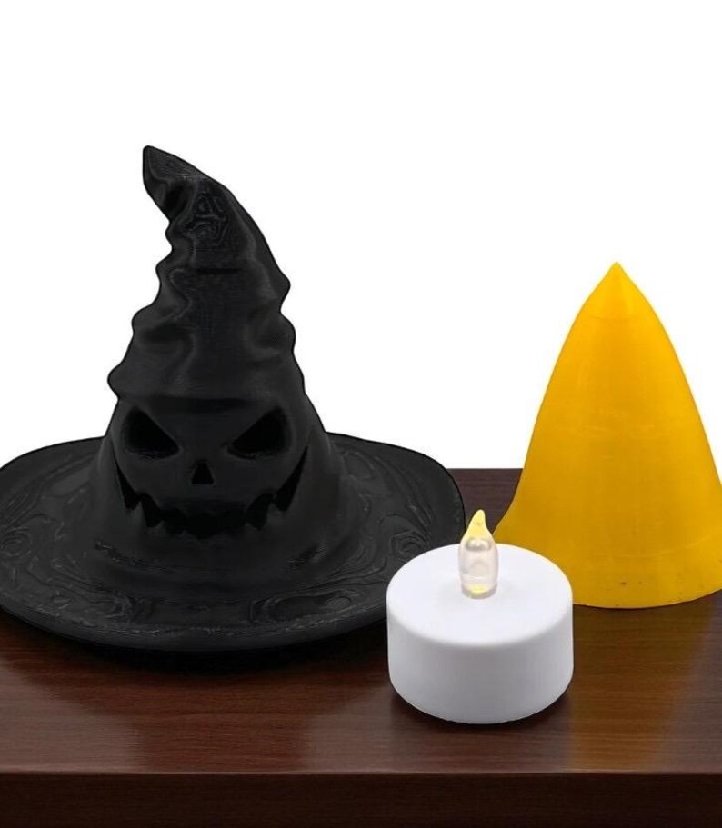 May include: A black Halloween witch hat with a carved jack-o'-lantern face, a yellow cone, and a white battery-operated candle with a flickering yellow flame. The items are arranged on a dark brown surface.