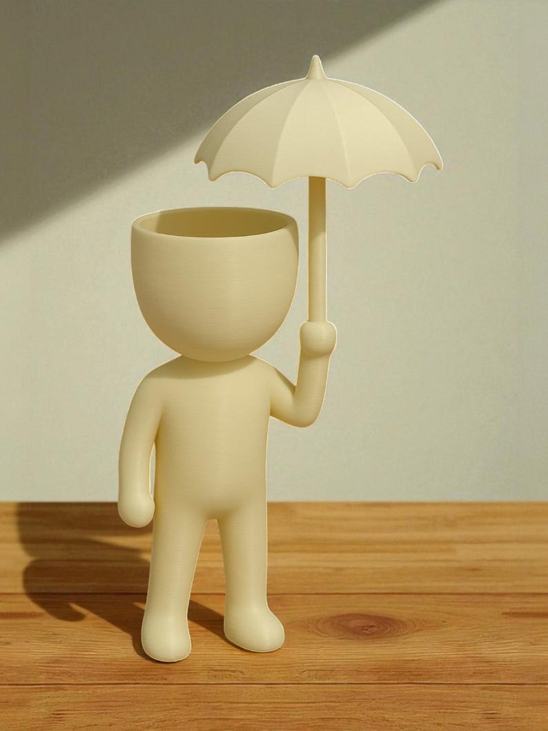 May include: A cream-colored figurine of a person holding an umbrella. The figure has a large, open head, functioning as a planter. The umbrella is also cream-colored, providing a whimsical design. The figurine stands on a wooden surface.