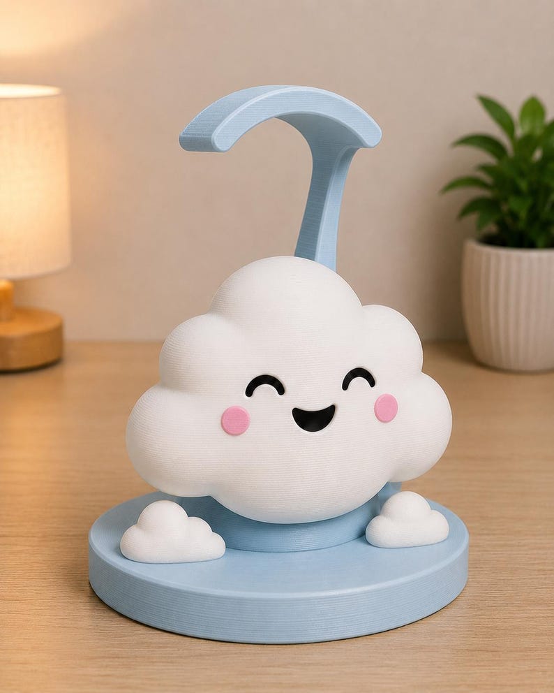 May include: A whimsical cloud-shaped night light in white and light blue. The cloud has a smiling face with pink cheeks and sits on a light blue base. A curved handle extends from the top. Decorative and functional.