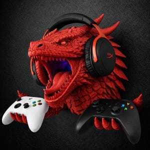 May include: A red dragon head wall mount featuring textured scales and an open mouth. The dragon wears black and orange over-ear headphones and uses its clawed hands to hold a white game controller on the left and a black game controller on the right.