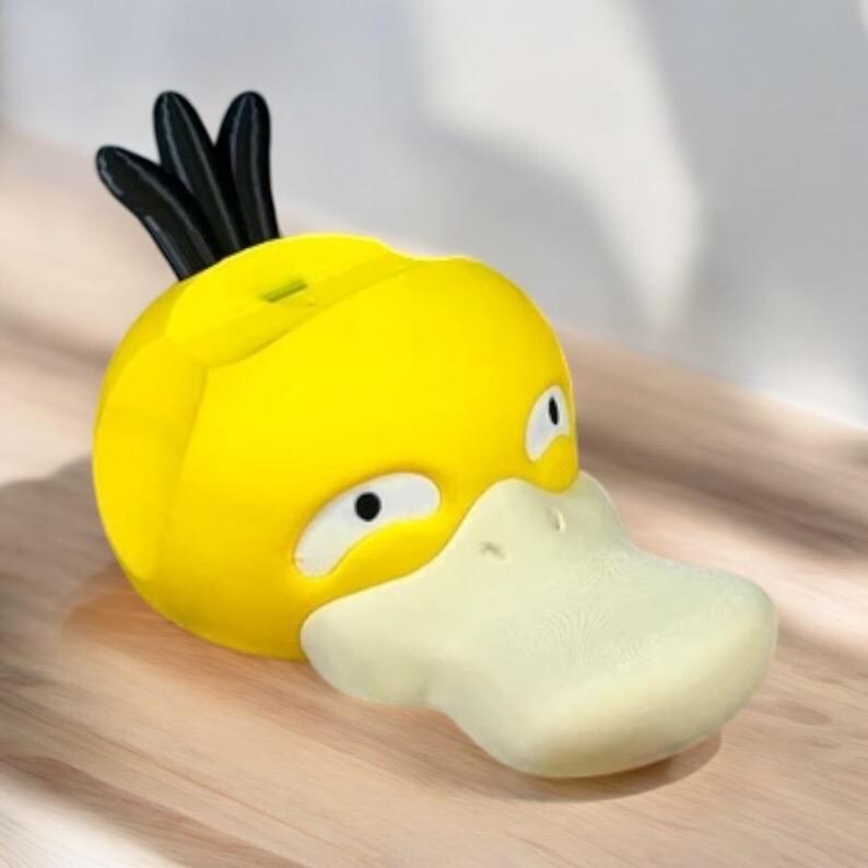 May include: A yellow, duck-shaped figurine with black accents and a light-colored beak. The figurine has a slot on top and is likely a coin bank or decorative item. The design is cartoonish and playful.