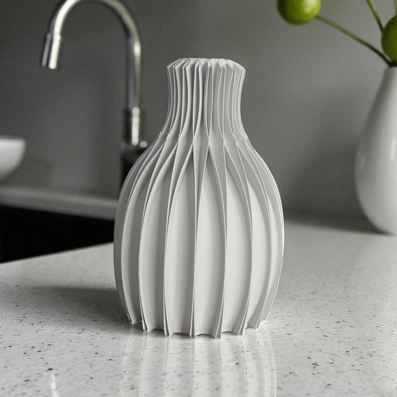 May include: A white, decorative vase with a unique, pleated design. The vase has a bulbous body and a narrow neck, with vertical pleats creating a textured surface. The vase is made of a solid, opaque material and is suitable for home decor.