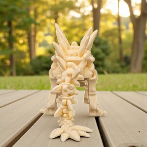 May include: A light beige, abstract sculpture with a complex, layered design. The sculpture has a central, upright structure with multiple protrusions and a smaller, detached piece in front. The sculpture is on a wooden deck.