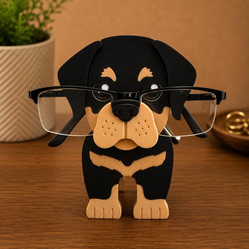 May include: A black and tan Rottweiler dog-shaped eyeglass holder. The holder is made of wood and has a black frame holding a pair of eyeglasses. The dog's face is tan with black accents, and the eyeglasses are clear.