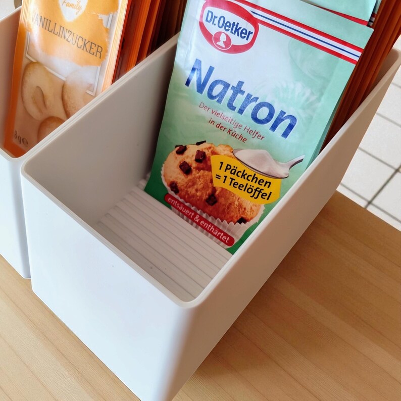 May include: A white plastic organizer with multiple compartments, holding packets of baking ingredients. One packet is labeled "Natron" by Dr. Oetker, with a picture of a muffin. Another packet is labeled "Vanillinzucker".