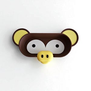 May include: A brown and yellow monkey-shaped wall-mounted shelf. The shelf has a rectangular shape with two large white eye-shaped openings, yellow ears, and a yellow nose. The shelf is designed to look like a monkey's face.