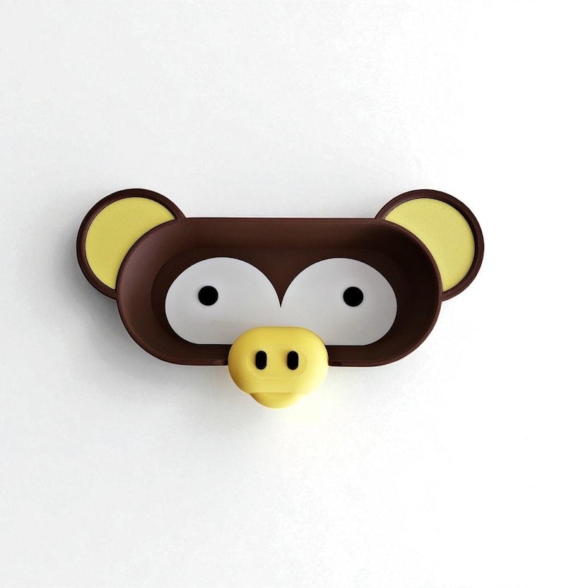 May include: A brown and yellow monkey-shaped wall-mounted shelf. The shelf has a rectangular shape with two large white eye-shaped openings, yellow ears, and a yellow nose. The shelf is designed to look like a monkey's face.
