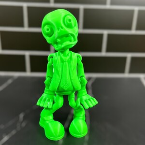 May include: A bright green 3D printed figurine of a zombie wearing a suit and tie. The zombie has a wide open mouth and large eyes.