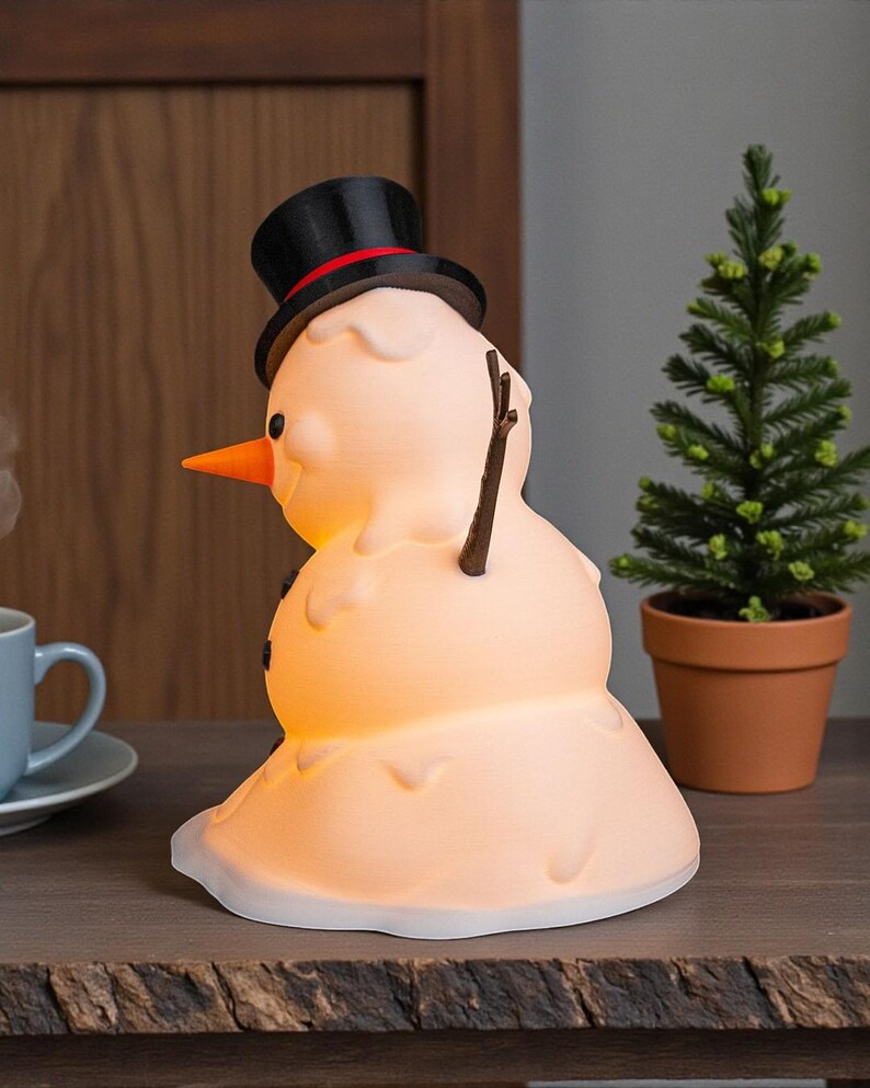 May include: A snowman-shaped lamp with a black top hat and an orange carrot nose. The lamp emits a warm, glowing light and has stick arms and black button eyes. A small potted evergreen tree is next to it.