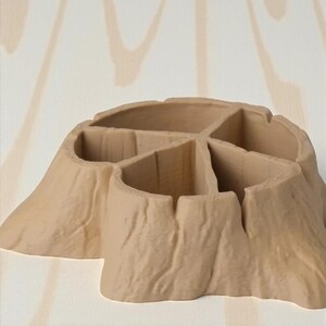 May include: A beige, tree stump-shaped desk organizer with multiple compartments. The organizer has a textured surface, resembling tree bark, and is designed to hold pens, pencils, or other small office supplies. The design is a unique and naturalistic addition to any desk.
