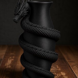 May include: A black vase with a dragon wrapped around it. The dragon's head is at the top, and its body coils around the vase. The vase has a textured surface and sits on a wooden surface.