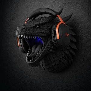 Puede incluir: Soporte de pared con cabeza de drag&oacute;n negro con auriculares naranjas y negros. La boca del drag&oacute;n est&aacute; abierta, revelando dientes afilados y una luz azul. Los auriculares tienen el logotipo de HyperX.