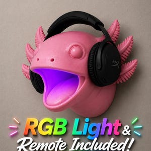 May include: A pink axolotl head sculpture with black headphones. The axolotl has feathery gills and an open mouth with a purple glow. The text "RGB Light & Remote Included!" is displayed in colorful letters.
