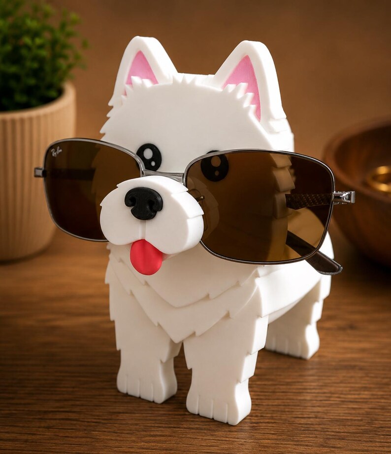 May include: A white dog-shaped sunglasses holder with pink-lined ears and a red tongue. The holder is wearing brown sunglasses. The dog is standing on a wooden surface. A small plant is in the background.
