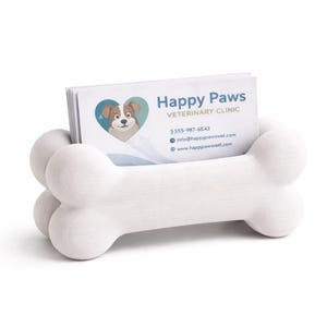 K&ouml;nnte beinhalten: Ein wei&szlig;er, knochenf&ouml;rmiger Visitenkartenhalter. Der Halter enth&auml;lt einen Stapel Visitenkarten mit dem Text "Happy Paws VETERINARY CLINIC" und einem Logo eines Hundes in einem Herzen. Kontaktinformationen sind ebenfalls sichtbar.