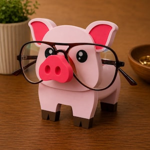 May include: A pink pig-shaped eyeglasses holder with a bright pink nose and ears. The holder has black eyes and brown feet. A pair of brown-framed glasses rests on the pig's nose, adding a touch of whimsy to this desk accessory.