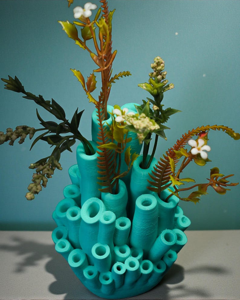 May include: A turquoise, coral-shaped vase with various openings, holding an assortment of artificial plants and flowers. The plants feature green, brown, and white accents, creating a vibrant contrast against the vase's color.