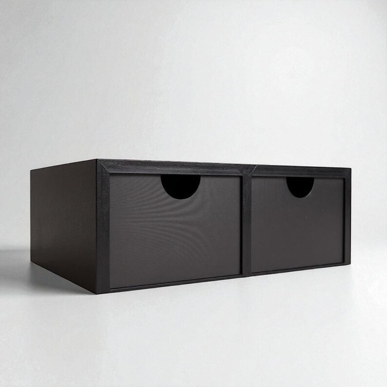 Pu&ograve; includere: Un mobile contenitore nero a due cassetti dal design minimalista. Ogni cassetto ha un'apertura semicircolare per una facile apertura. L'unit&agrave; &egrave; realizzata in un materiale scuro ed &egrave; adatta a varie esigenze di stoccaggio.