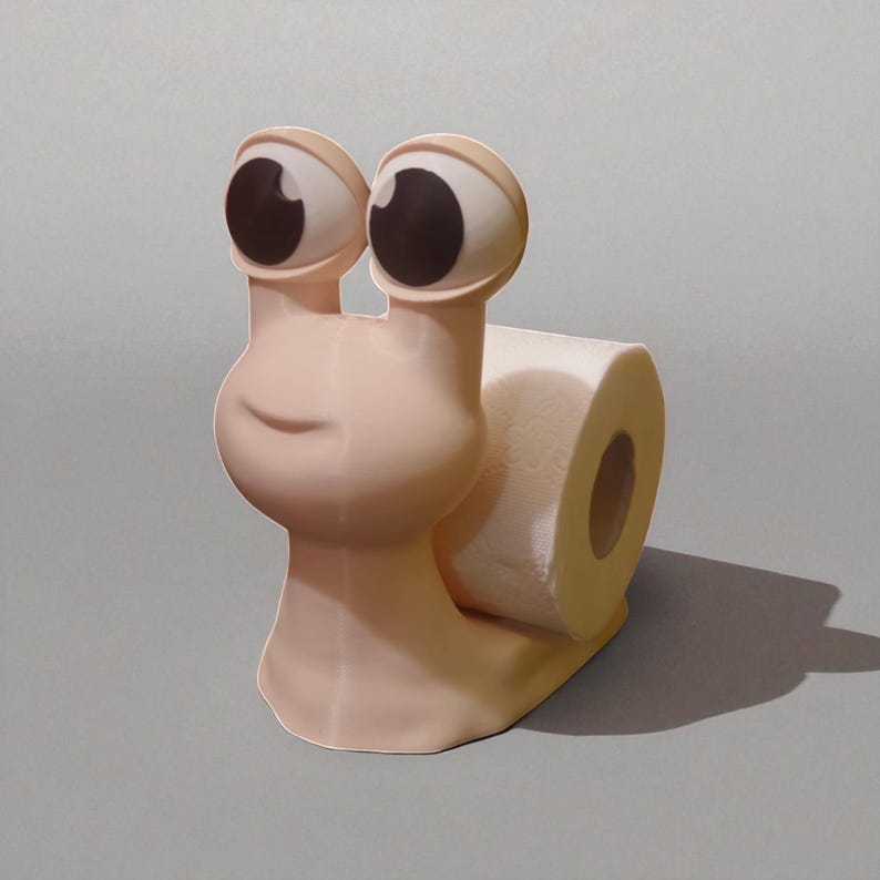 May include: A whimsical, light pink snail-shaped toilet paper holder. The snail has large, cartoonish eyes with brown pupils and a smiling face. A roll of white toilet paper is held in the snail's shell. The holder is on a gray surface.
