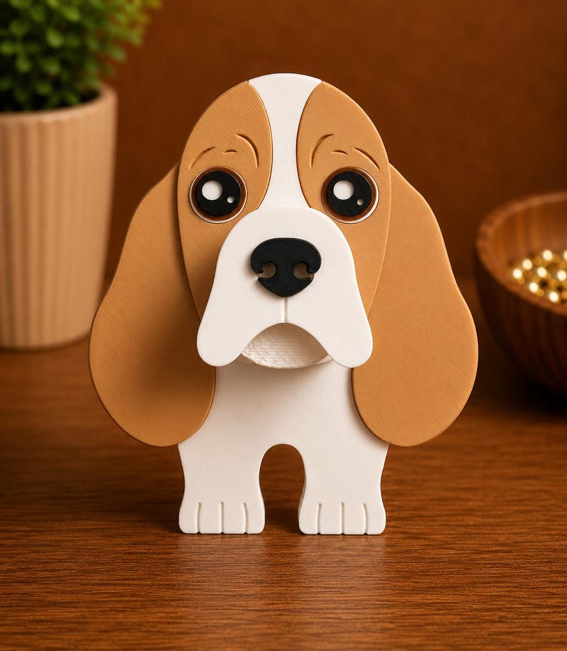 May include: A decorative dog figurine with a brown and white color scheme. The dog has large, expressive eyes, floppy ears, and a black nose. The figurine is made of layered materials and stands upright on a wooden surface.