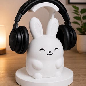 May include: A white bunny-shaped headphone stand with a smiling face, holding black headphones. The stand is on a round base. The headphones are black and have the brand name "SONY" on the side.