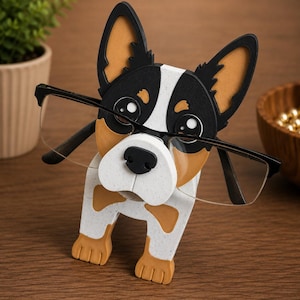 May include: A wooden eyeglasses holder shaped like a dog. The dog has black, white, and tan markings, with large ears and a black nose. The holder is designed to hold a pair of eyeglasses.