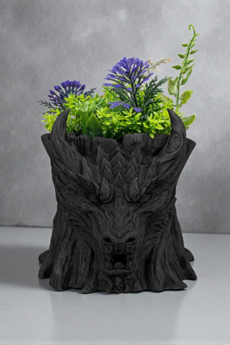 May include: A black, dragon-themed planter pot filled with artificial purple and green plants. The pot is sculpted with a detailed dragon face and textured bark-like appearance, creating a unique decorative piece.