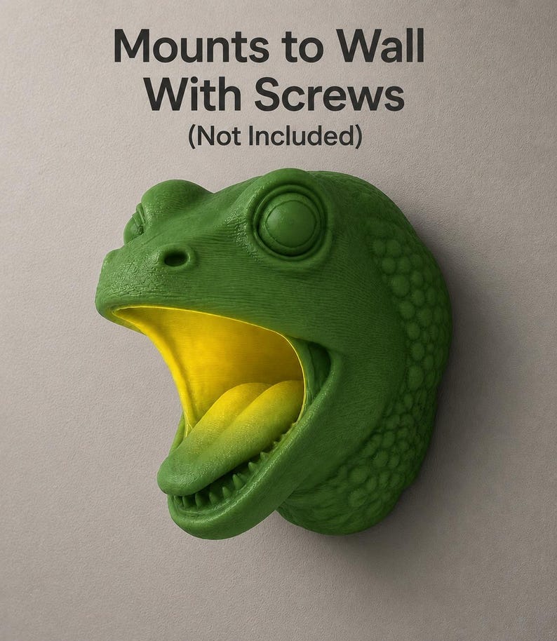 Op de afbeelding: Een groene dinosaurushoofdwandmontage met een gele binnenkant van de mond en tong. De kop is getextureerd en heeft een wijd open mond. De tekst "Mounts to Wall With Screws (Not Included)" staat bovenaan.
