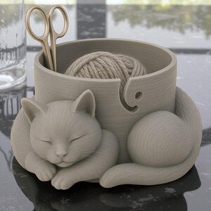 May include: A gray cat-shaped yarn bowl with a ball of yarn inside. The cat is curled up, with its eyes closed. A pair of gold scissors is placed in the bowl. The bowl has a hole for the yarn to feed through.