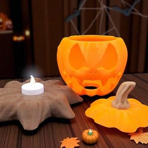 May include: Orange pumpkin-shaped candle holder with a carved face, a small pumpkin, and a decorative leaf. A lit white candle sits on a brown, star-shaped base. Halloween-themed decor.