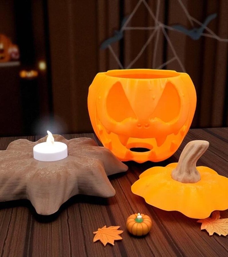 May include: Orange pumpkin-shaped candle holder with a carved face, a small pumpkin, and a decorative leaf. A lit white candle sits on a brown, star-shaped base. Halloween-themed decor.