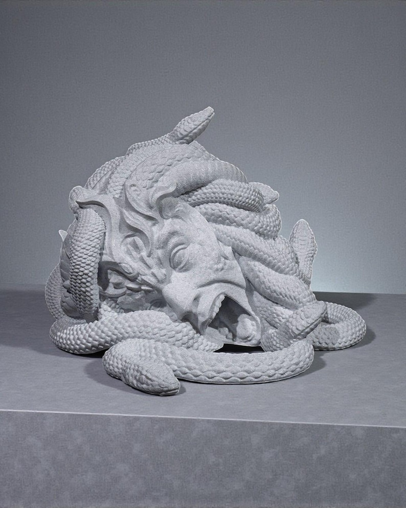 Peut inclure: Une sculpture grise de la t&ecirc;te de M&eacute;duse, avec des serpents s'enroulant autour du visage et de la t&ecirc;te. La sculpture a une bouche ouverte et des traits faciaux d&eacute;taill&eacute;s. L'&oelig;uvre est expos&eacute;e sur une surface grise.