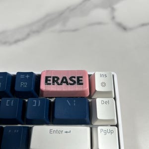 May include: A pink keyboard key with the word "ERASE" printed in black letters.