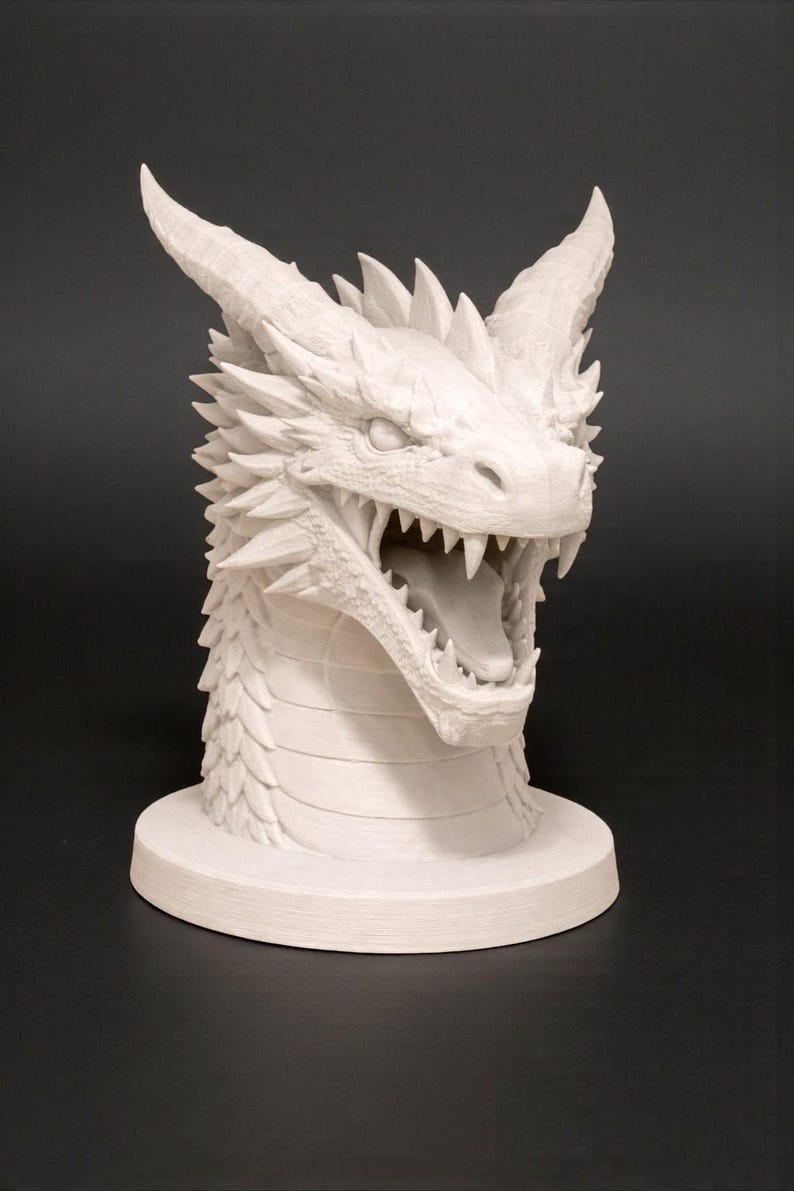 May include: A white dragon head sculpture with an open mouth, revealing sharp teeth and a long tongue. The sculpture has detailed scales, horns, and a spiky mane. The dragon head is mounted on a round base.