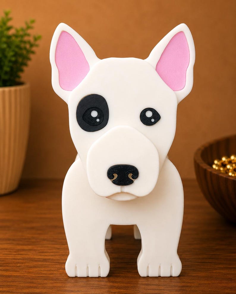 May include: A white dog figurine with pink inner ears and a black eye patch. The dog has a black nose and is standing on four legs. The figurine is made of a smooth material and is set against a brown background.
