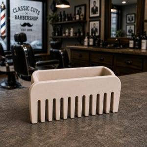 Puede incluir: Un organizador beige en forma de peine, probablemente para una barber&iacute;a. Tiene forma rectangular con ranuras verticales que se asemejan a los dientes de un peine. El fondo muestra una barber&iacute;a con sillas, espejos y el texto "CLASSIC CUTS BARBERSHOP".