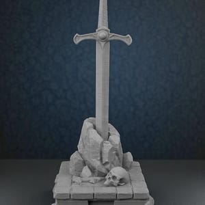 May include: A gray sculpture of a sword in a stone, with a skull at the base. The sword has a detailed hilt and is set in a rocky formation atop a rectangular base. The overall design evokes a fantasy theme.