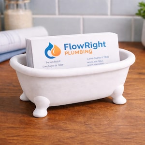 May include: A white ceramic bathtub-shaped business card holder. The holder contains a stack of white business cards with the "FlowRight Plumbing" logo. The holder sits on a wooden surface.