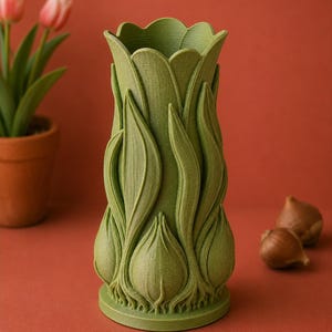 May include: A green, tulip-shaped vase with a textured surface. The vase has a detailed design of tulip leaves and bulbs. The vase is on a red-orange surface, with a potted plant and tulip bulbs in the background.